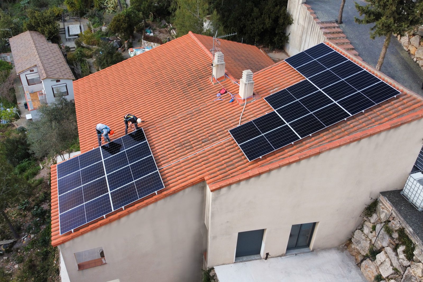 Dos instaladores colocando placas solares sobre el tejado de teja de una vivienda de Vallirana