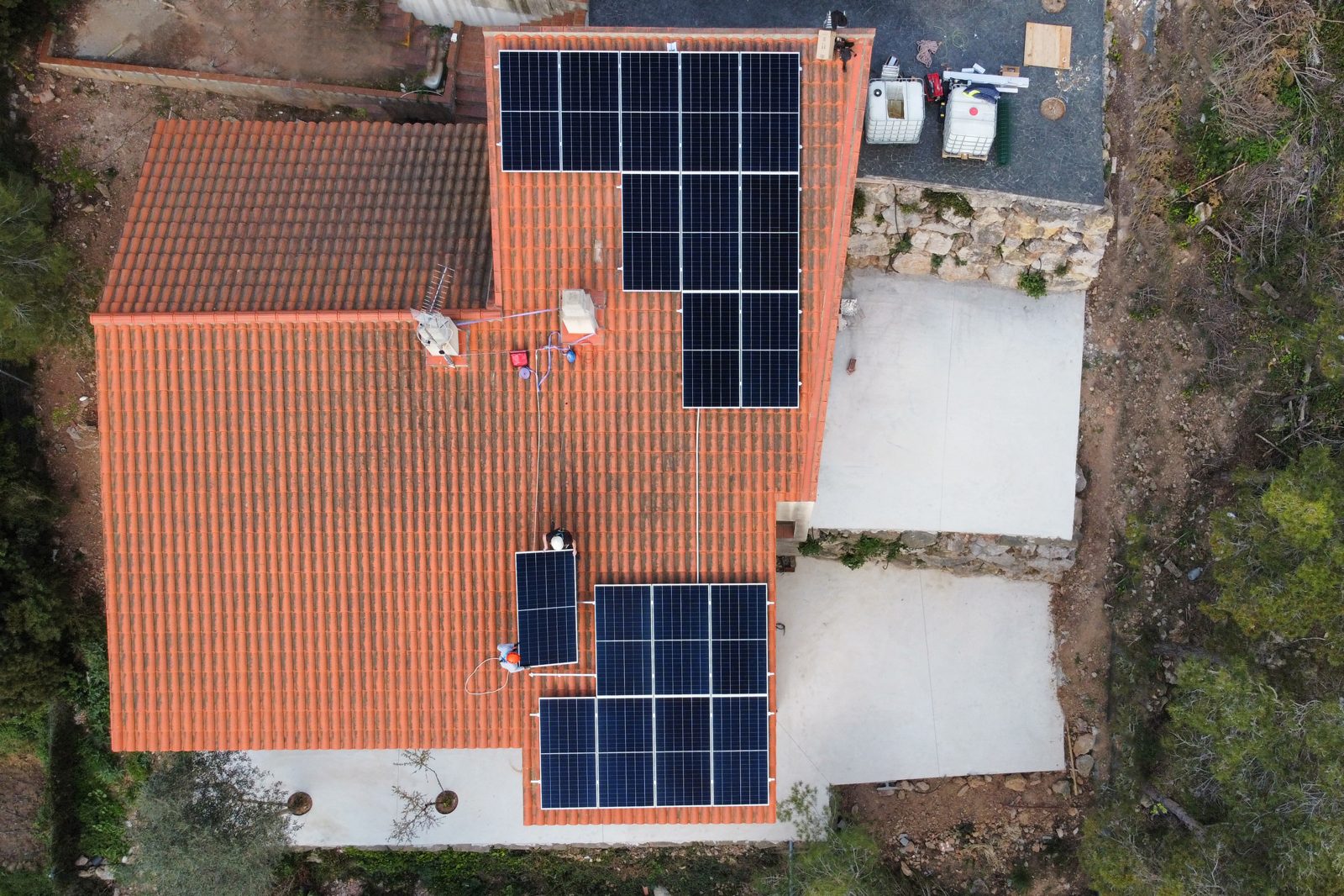 Vista cenital de la cubierta de una vivienda de Vallirana con placas solares y dos instaladores subiendo un módulo